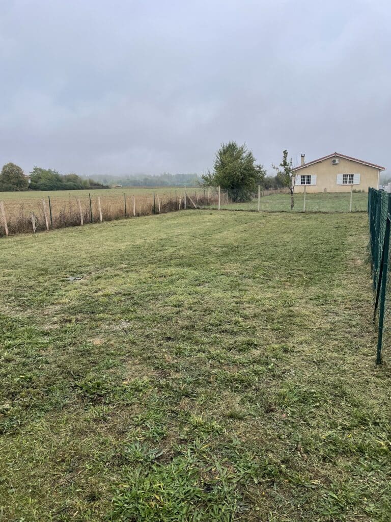 Jardin avec pelouse tondue et maison de campagne Grand jardin tondu avec clôture, maison de campagne au toit rouge et paysage brumeux en arrière-plan.